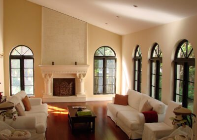 Elegant living room with arched windows, cream walls, white sofas, hardwood floor, and a large stone fireplace.