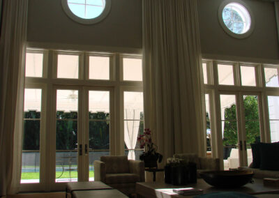Bright living room with tall windows, round upper windows, white curtains, and modern furniture in soft sunlight.