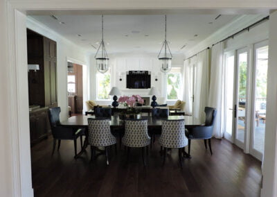 Modern dining room with patterned chairs, dark table, pendant lights, large windows, and a TV on a white wall.