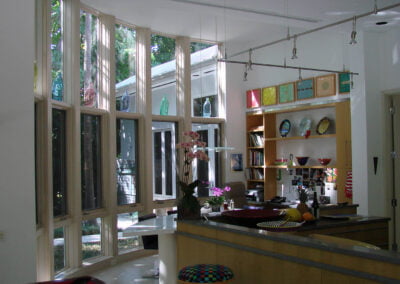 Modern kitchen with tall, angled windows, open shelves, plants, colorful decor, and natural light streaming inside.